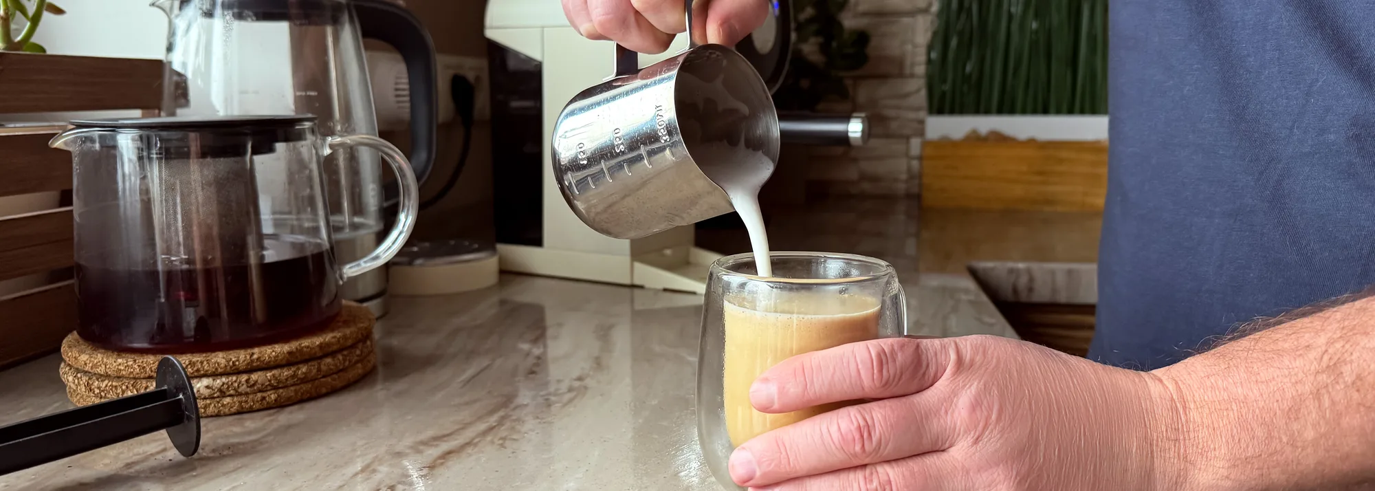 Manos de un hombre vertiendo leche en un vaso de café con leche sobre una encimera de piedra