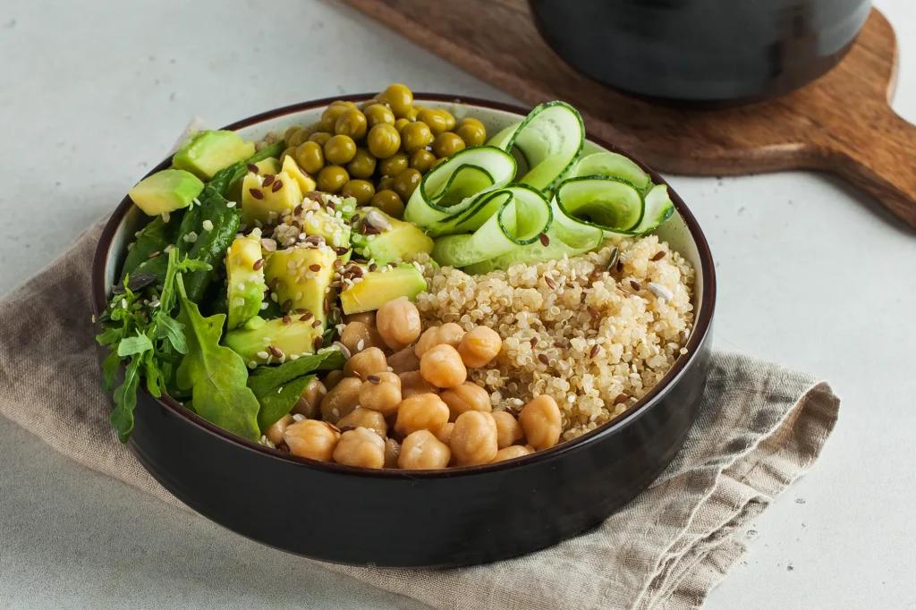 Bol con garbanzos, quinoa, aguacate, guisantes y pepino en tiras sobre un paño de lino