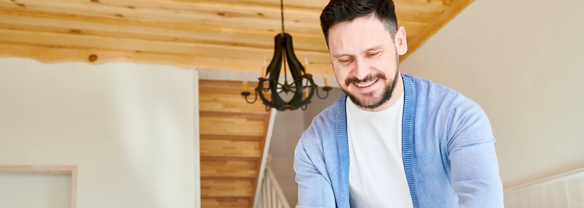 Hombre sonriente con chaqueta azul preparando la mesa para comer en un comedor luminoso de madera